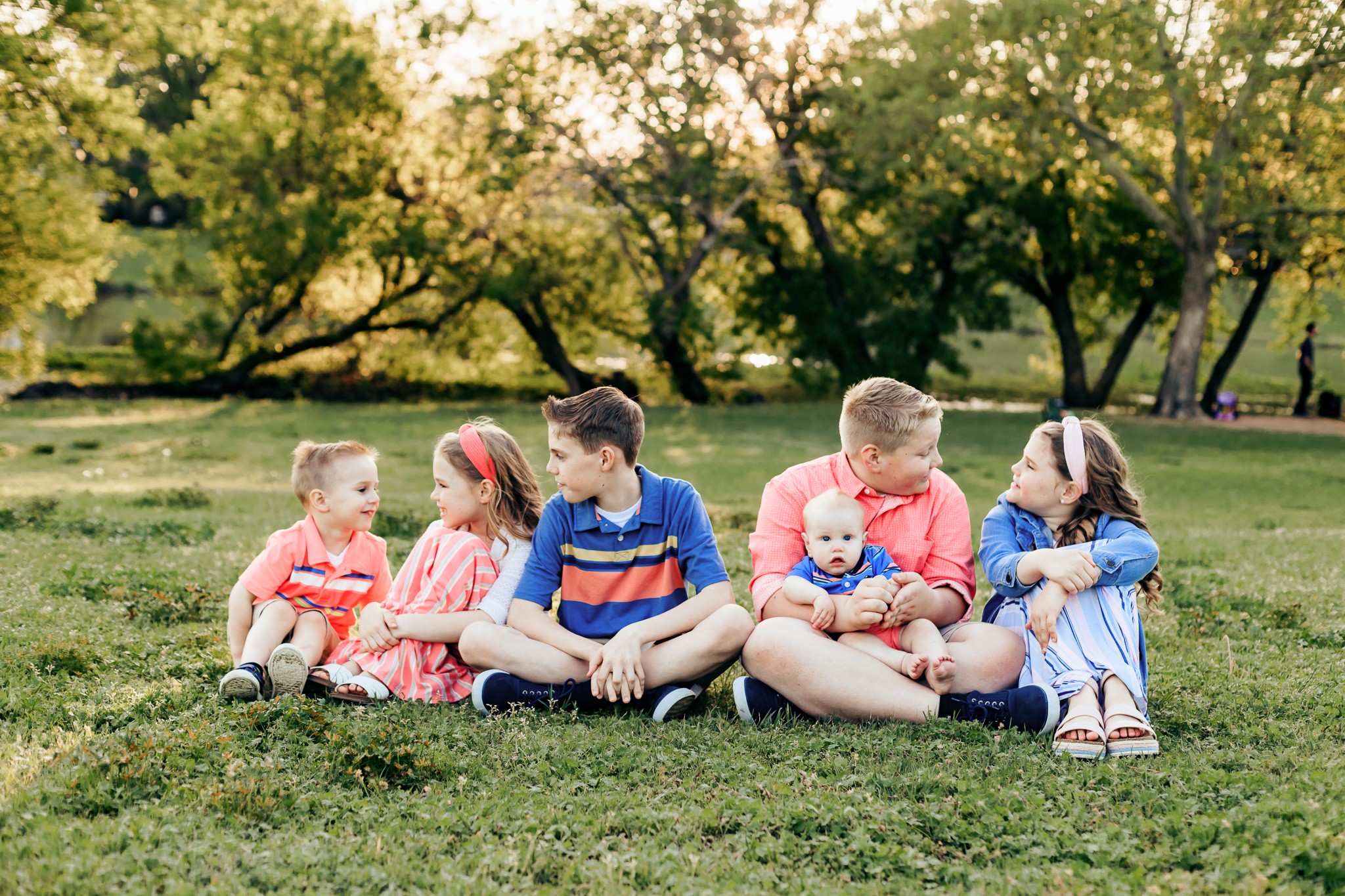 6 siblings sit together on the grass during golden hour. 