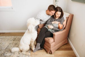 A photo of new parents, new baby and their poodle.