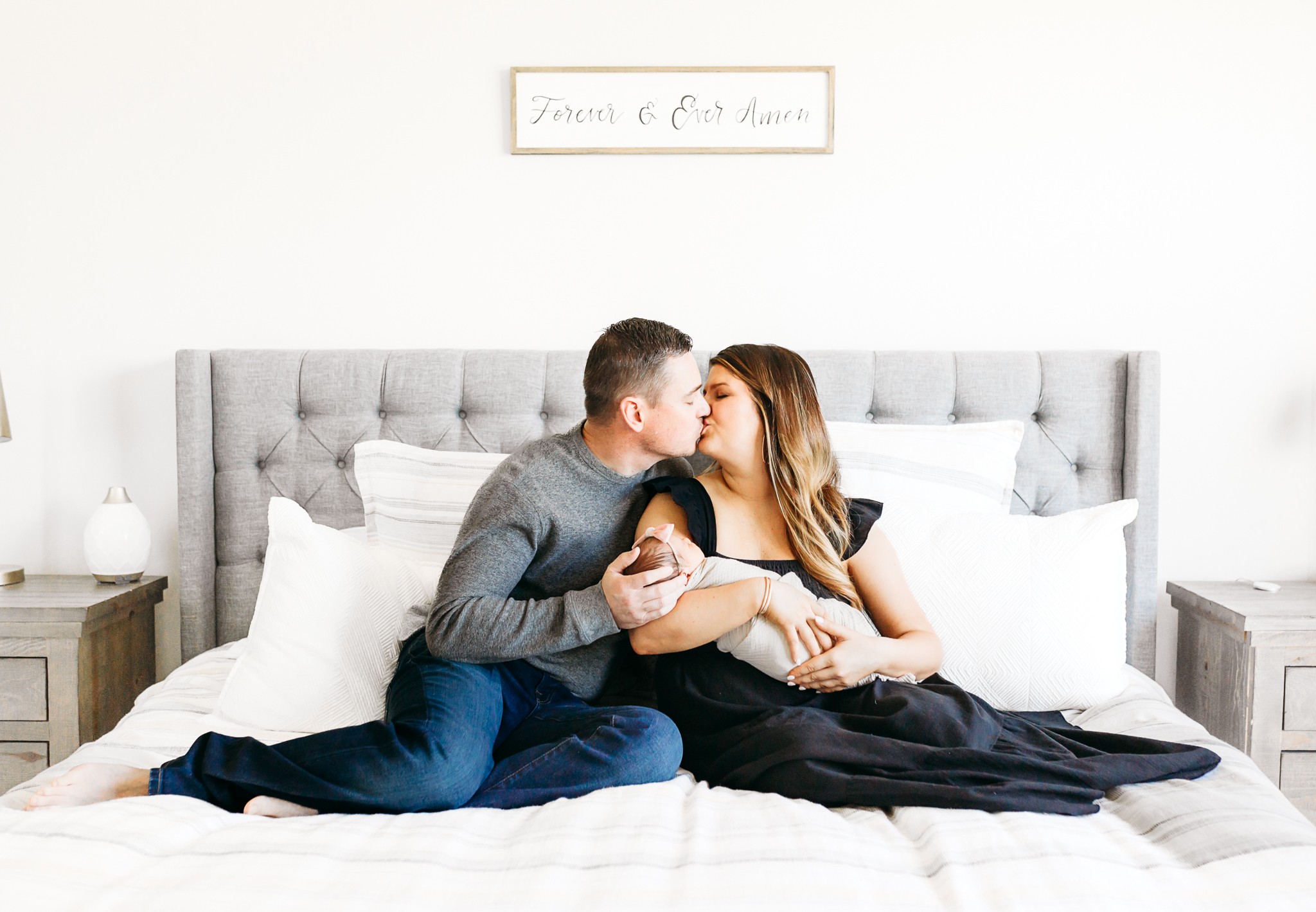 New parents sit on bed during at home newborn photo session.