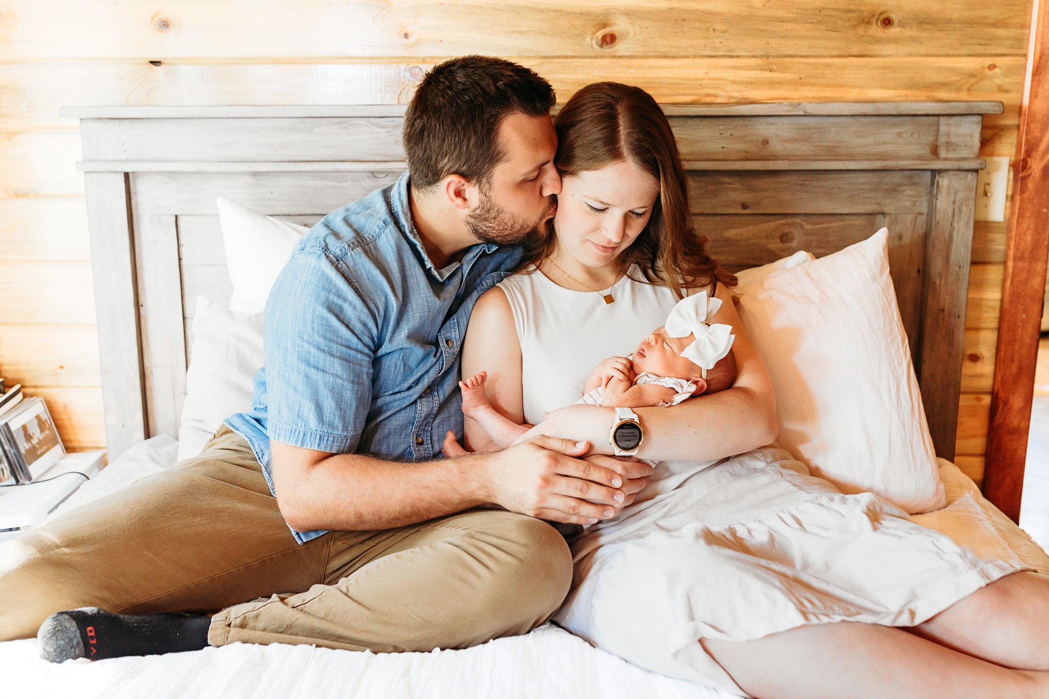 Mom and Dad sit on bed with newborn during OKC newborn photoshoot.